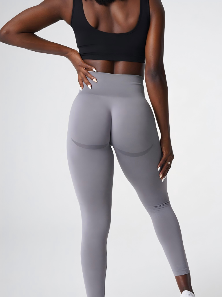 Woman wearing a black sports bra and gray leggings, posing with a hand on her hip, showing a back view.