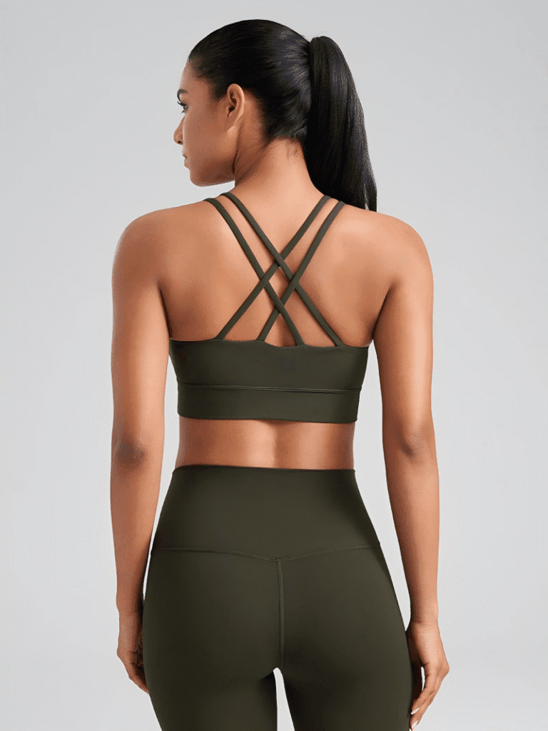 Woman wearing a dark olive green sports bra with criss-cross straps on the back, paired with matching leggings