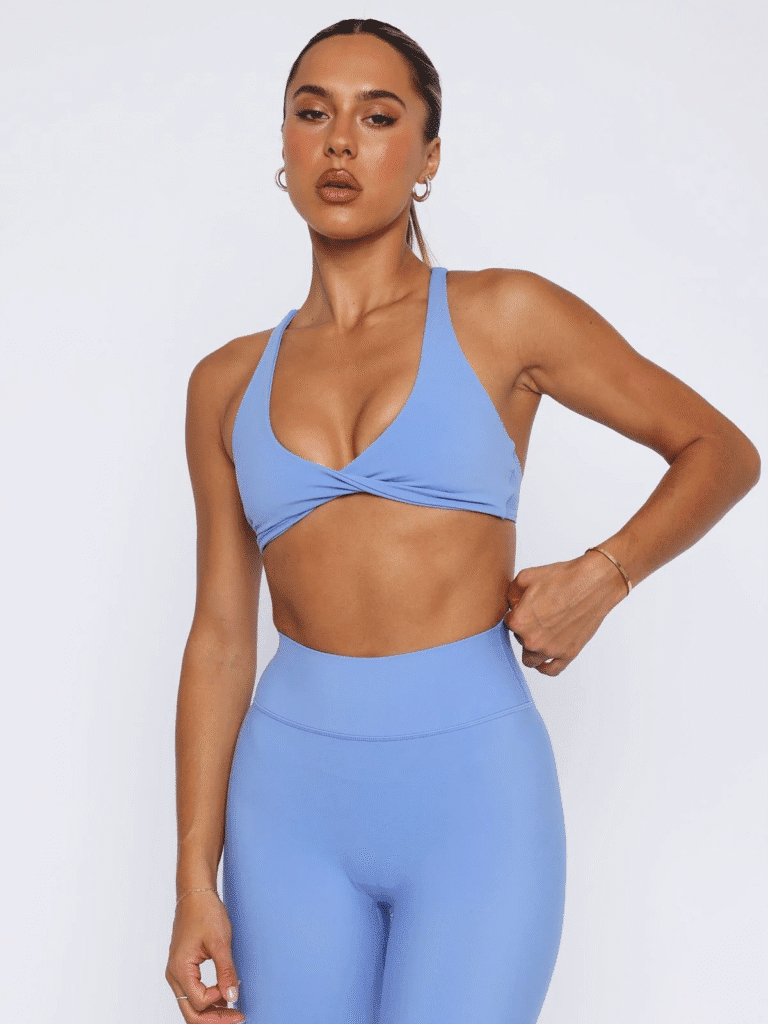 Woman wearing a light blue twisted front sports bra and matching high-waisted leggings, posing confidently.