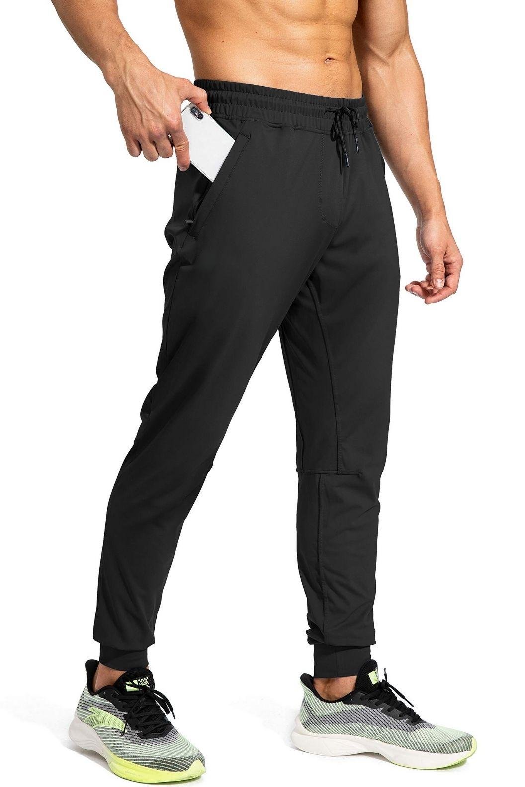 A man in black athletic pants and sneakers holds a smartphone in his pocket, showcasing his activewear.