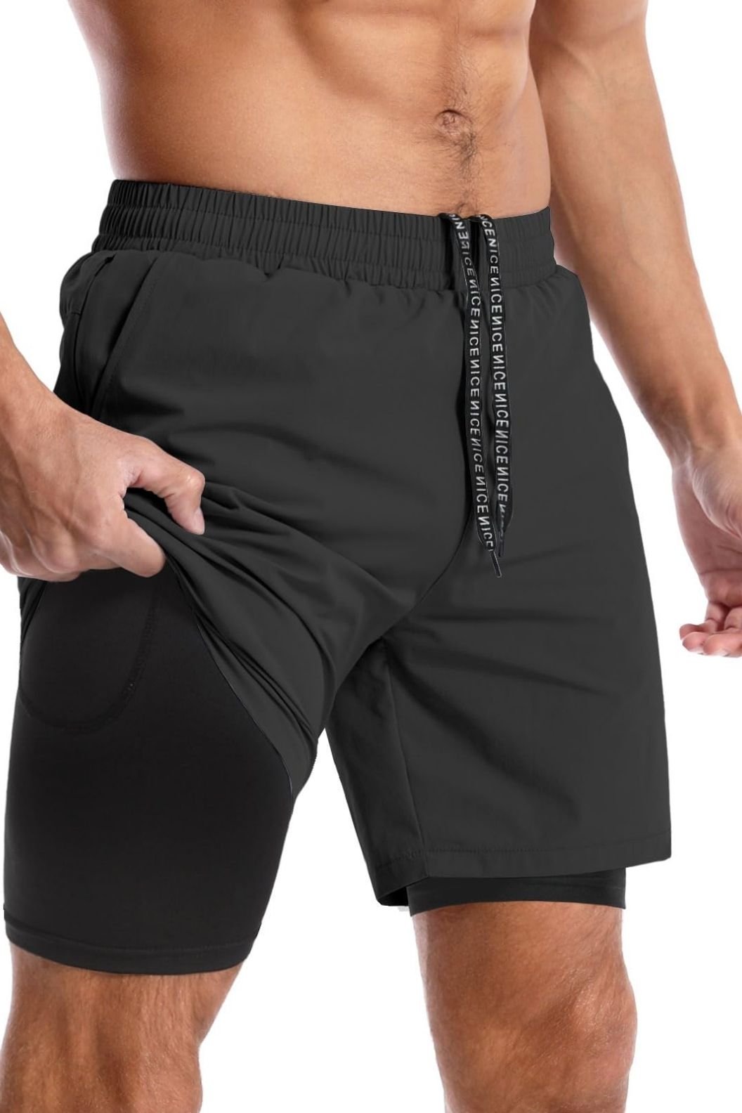 A man adjusts the waistband of his black athletic shorts, revealing the inner layer of compression shorts.