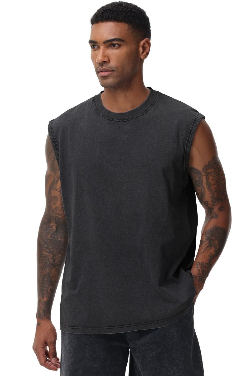 A man in a sleeveless black t-shirt with tattoos on his arms, standing in a relaxed pose.