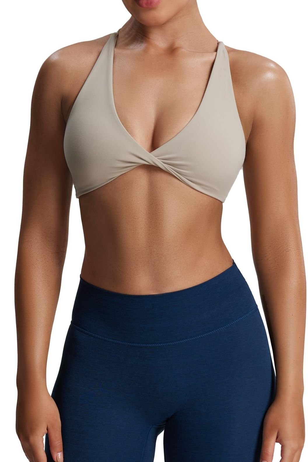 A woman in a beige sports bra and blue leggings, showcasing her toned midriff.