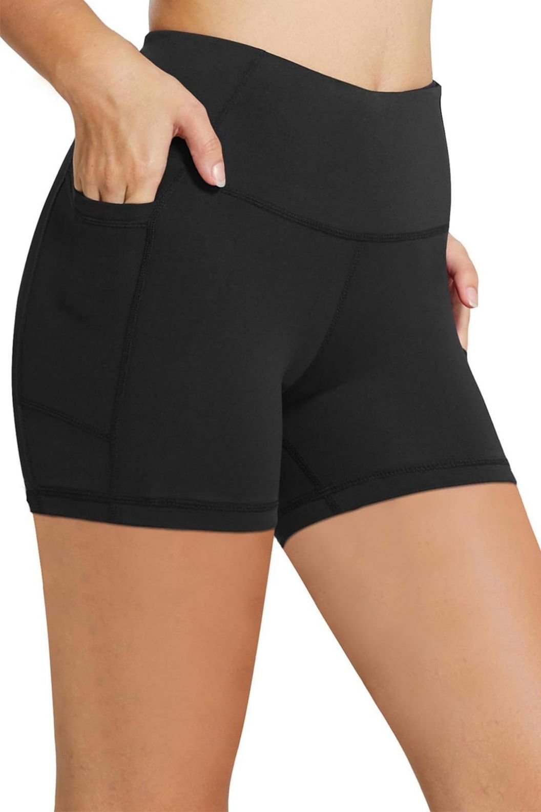 A woman in black workout shorts with pockets, placing her hand in one of the pockets.