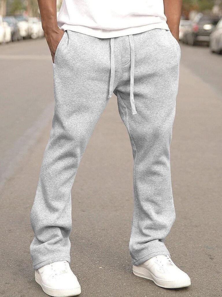 Man wearing light gray sweatpants with drawstring waist and white sneakers on city street.